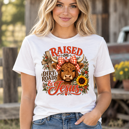 Model wearing a white Raised on Dirt Roads and Jesus Highland cow graphic T-shirt